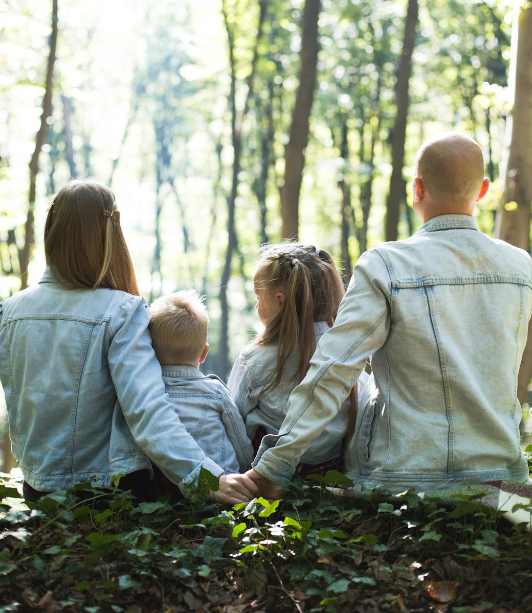 Une famille assise en forêt, de dos, les parents entourant leurs deux enfants